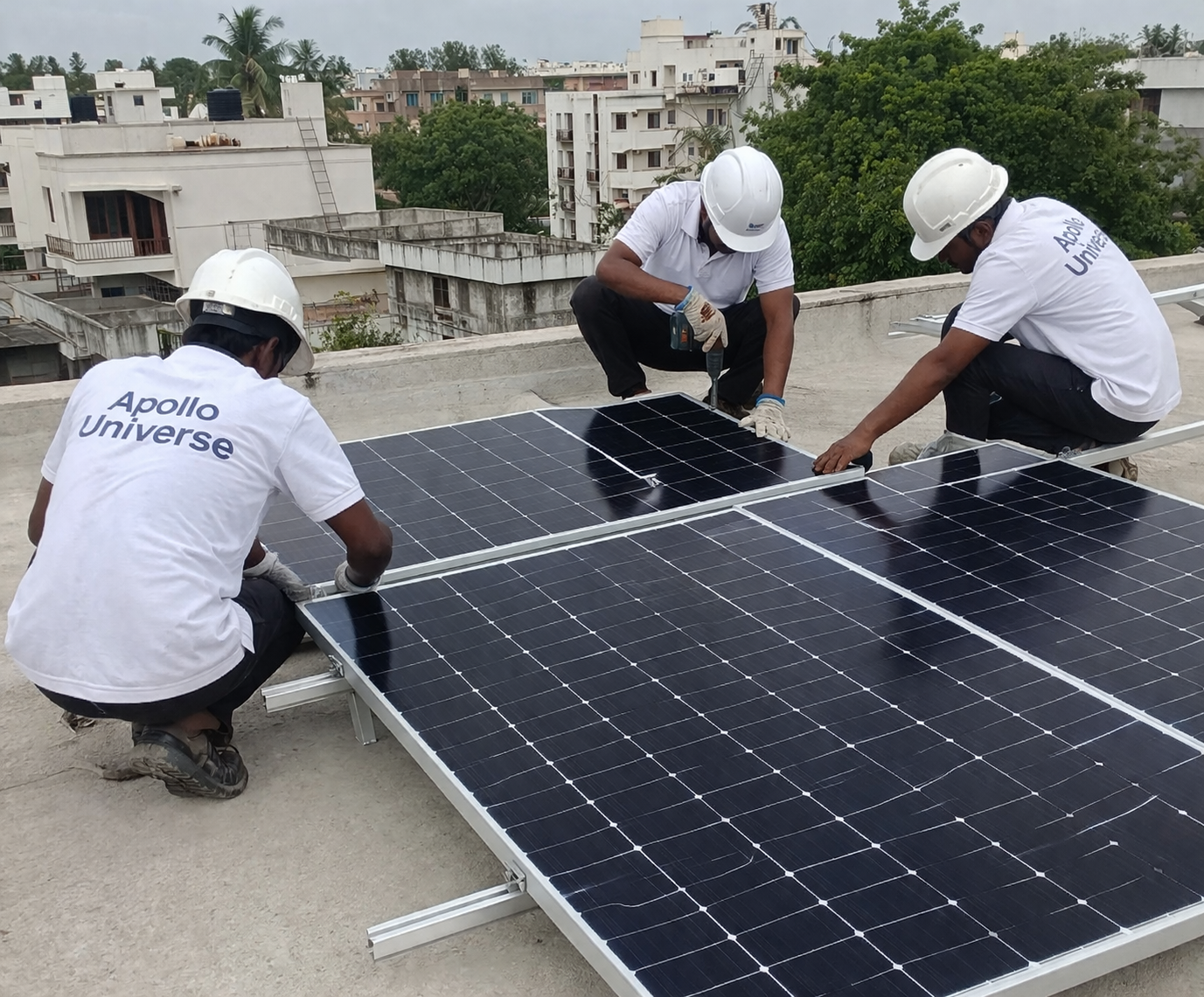 "Three technicians wearing safety helmets and white Apollo Universe T-shirts installing 1 kW solar panels on a residential rooftop using mounting structure."